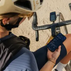 Jaka nawigacja na rower? Kolarz sprawdza dane treningowe na telefonie i liczniku rowerowym, planując dalszą trasę.