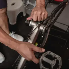 Ręce majsterkowicza przy rowerze, pokazujące, jak zdjąć korbę. Widoczne narzędzia i elementy mechanizmu korbowego.