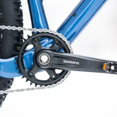 Widok z bliska na niebieski rower, z widoczną korbą Shimano i łańcuchem. Dowiedz się, jak odkręcić pedały w rowerze.