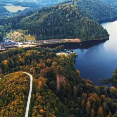 Malownicze jezioro Bystrzyckie otoczone lasami, z krętą drogą wijącą się po zboczu i zabudowaniami nad brzegiem.