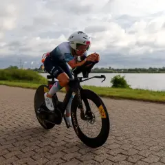 Kolarski wyścig inaczej: zawodniczka w aerodynamicznej pozycji na rowerze czasowym, ścigająca się wzdłuż jeziora.
