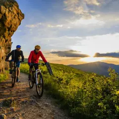 Dwóch rowerzystów przemierza górski szlak o zachodzie słońca, odkrywając piękno krajoznawstwa.