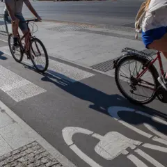 Ludzie na rowerach jadą ścieżką rowerową z oznaczeniem art 33 prd. Cienie rzucane przez rowerzystów wydłużają się na asfalcie.