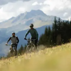 Dwóch rowerzystów zjeżdża po zboczu w Tatrach, podziwiając wielką siklawę w oddali.