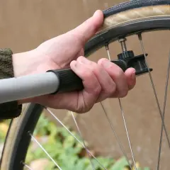 Dłoń trzyma pompkę przy wentylu koła rowerowego 26 cali. Sprawdzanie, jakie ciśnienie w oponach rowerowych 26 cali, jest kluczowe dla komfortu jazdy.