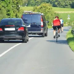 Rowerzyści na drodze, przestrzegający przepisy ruchu drogowego dla rowerzystów, mijani przez samochody i vana.