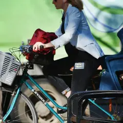 Kobieta na rowerze z koszykiem, w tle zielony ekran. Widać naszywkę z Batmanem na jej spodniach. To może być region z Popradem, gdzie można podziwiać piękne krajobrazy.