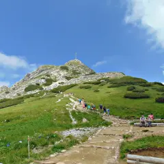 Tłum ludzi wspina się po kamienistym szlaku na Giewont. Widać krzyż na szczycie.