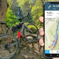 Rower gravelowy przy wodospadzie, a obok smartfon z aplikacją komoot pokazującą trasę i dystans.