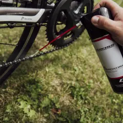 Dłoń trzyma puszkę z odtłuszczaczem do rowerów, aplikując go na łańcuch. Czy benzyna ekstrakcyjna odtłuszcza? Ten spray na pewno tak!