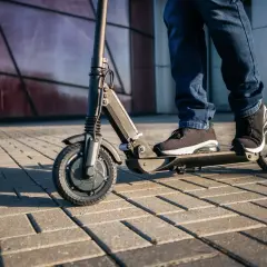 Osoba na hulajnodze elektrycznej jedzie po chodniku. Czy hulajnogą można jeździć po ścieżce rowerowej? To zależy od przepisów.