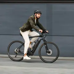 Mężczyzna w kasku i marynarce odbywa szybką jazdę wzdłuż po chodniku na rowerze elektrycznym.