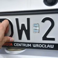 Dłoń przykłada tablicę rejestracyjną na bagażnik rowerowy. Widoczne litery DW i cyfry 29.