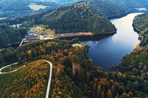 Malownicze jezioro Bystrzyckie otoczone lasami, z krętą drogą wijącą się po zboczu i zabudowaniami nad brzegiem.