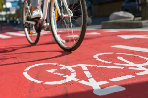 Rowerzysta nabiera prędkości na czerwonej ścieżce rowerowej, gdzie białe symbole rowerów wyznaczają trasę.