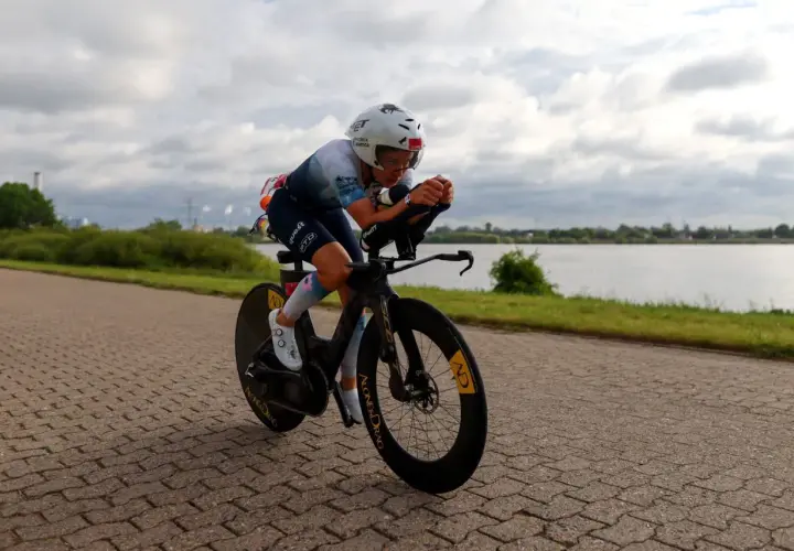 Kolarski wyścig inaczej: zawodniczka w aerodynamicznej pozycji na rowerze czasowym, ścigająca się wzdłuż jeziora.