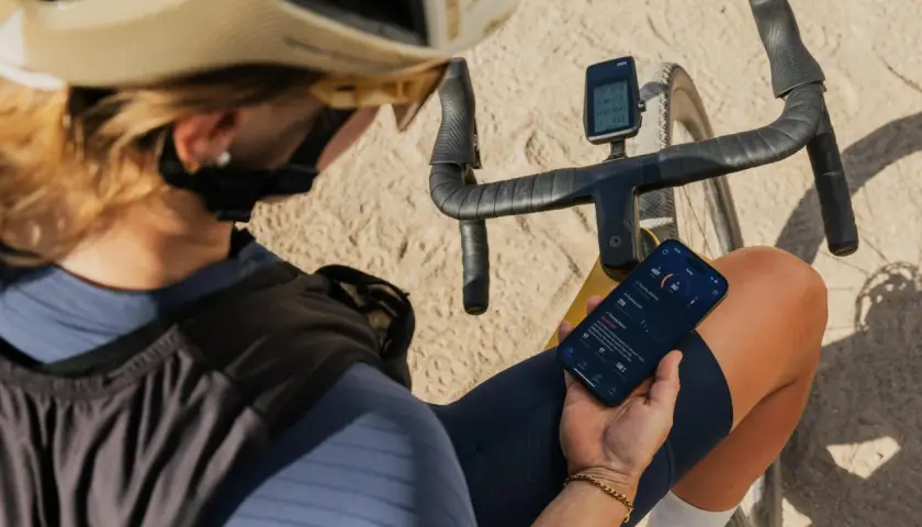 Jaka nawigacja na rower? Kolarz sprawdza dane treningowe na telefonie i liczniku rowerowym, planując dalszą trasę.