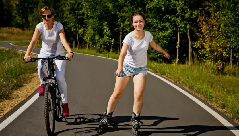 Dziewczyna na rolkach i kobieta na rowerze korzystają ze ścieżki rowerowej.