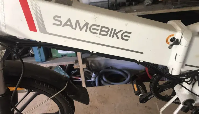 Biały rower elektryczny SAMEBIKE, z czerwonym i szarym paskiem, stoi w warsztacie. Wspomaganie nie działa, co jest frustrujące.