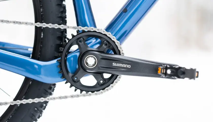 Widok z bliska na niebieski rower, z widoczną korbą Shimano i łańcuchem. Dowiedz się, jak odkręcić pedały w rowerze.