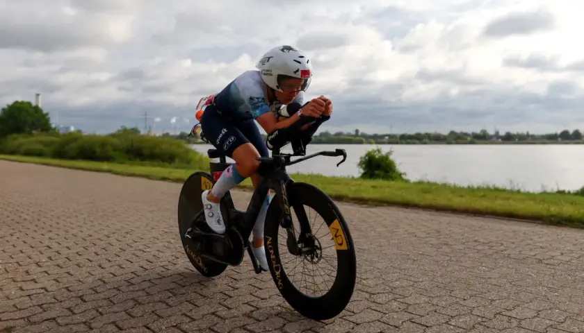 Kolarski wyścig inaczej: zawodniczka w aerodynamicznej pozycji na rowerze czasowym, ścigająca się wzdłuż jeziora.