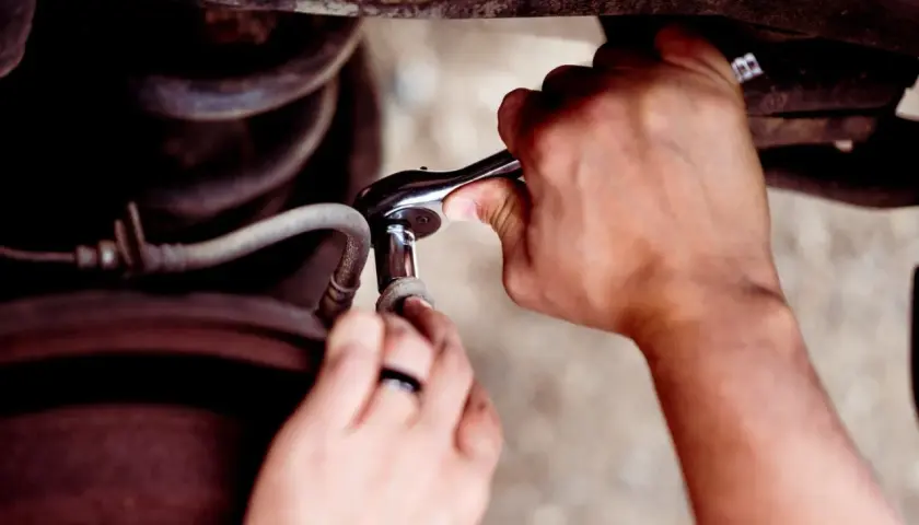 Ręce z kluczem nasadowym próbują odkręcić wyrobioną śrubę imbusową, która jest częścią mechanizmu samochodowego.