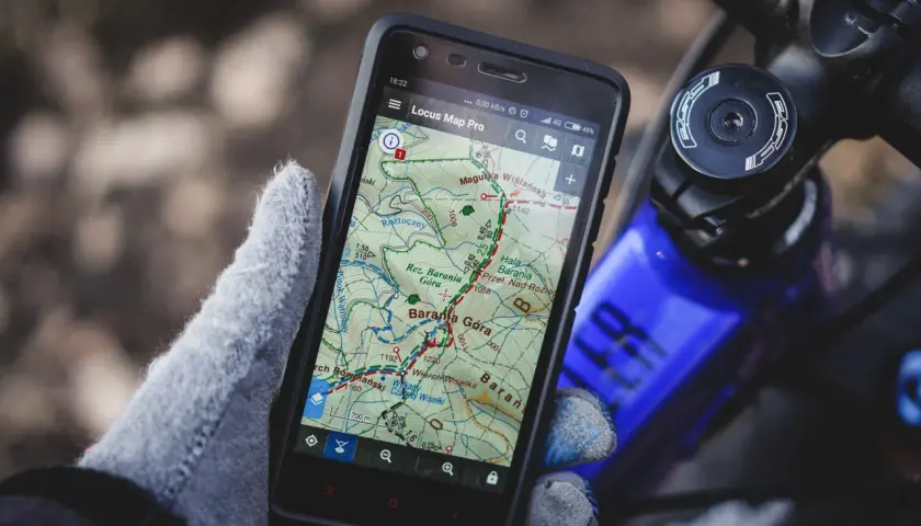 Rękawica trzyma smartfon z aplikacją szlaki turystyczne Locus Map Pro, pokazującą trasę w górach.