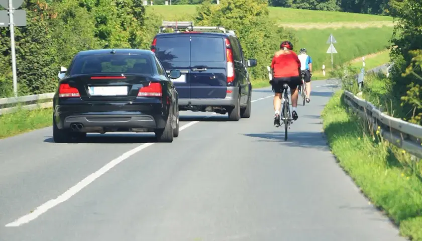 Rowerzyści na drodze, przestrzegający przepisy ruchu drogowego dla rowerzystów, mijani przez samochody i vana.