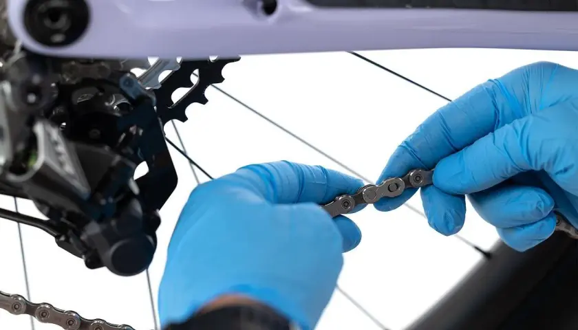 Ręce w niebieskich rękawiczkach dokonują wymiany łańcucha rowerowego, przygotowując go do montażu.