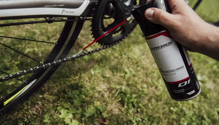 Dłoń trzyma puszkę z odtłuszczaczem do rowerów, aplikując go na łańcuch. Czy benzyna ekstrakcyjna odtłuszcza? Ten spray na pewno tak!
