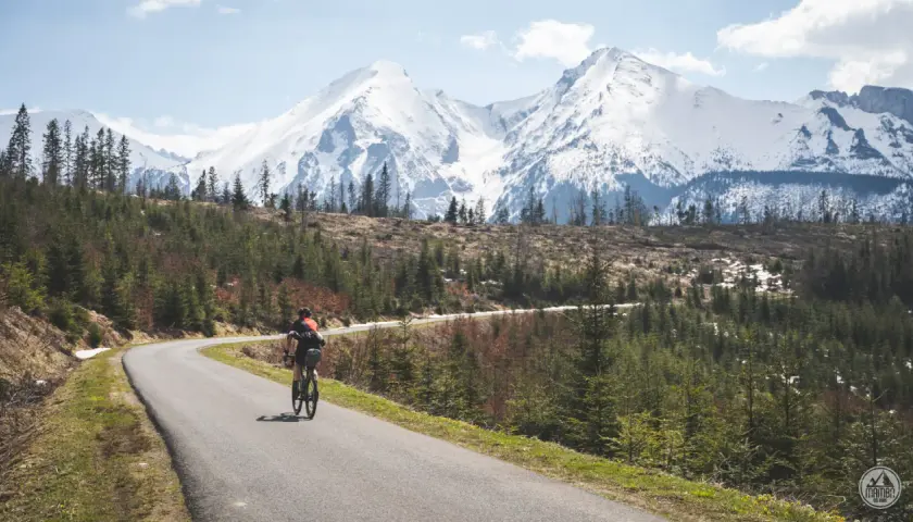 Rowerzysta na krętej drodze z widokiem na ośnieżone Tatry. Marzenie o rowerem dookoła Tatr w jeden dzień staje się rzeczywistością.