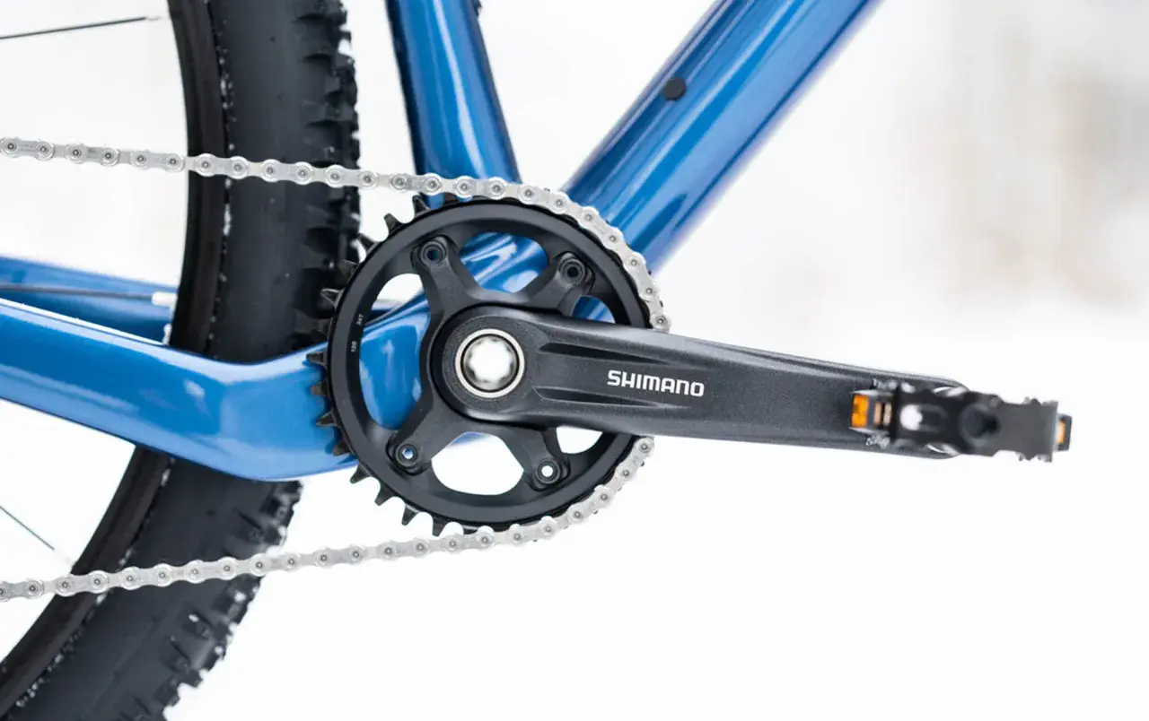 Widok z bliska na niebieski rower, z widoczną korbą Shimano i łańcuchem. Dowiedz się, jak odkręcić pedały w rowerze.