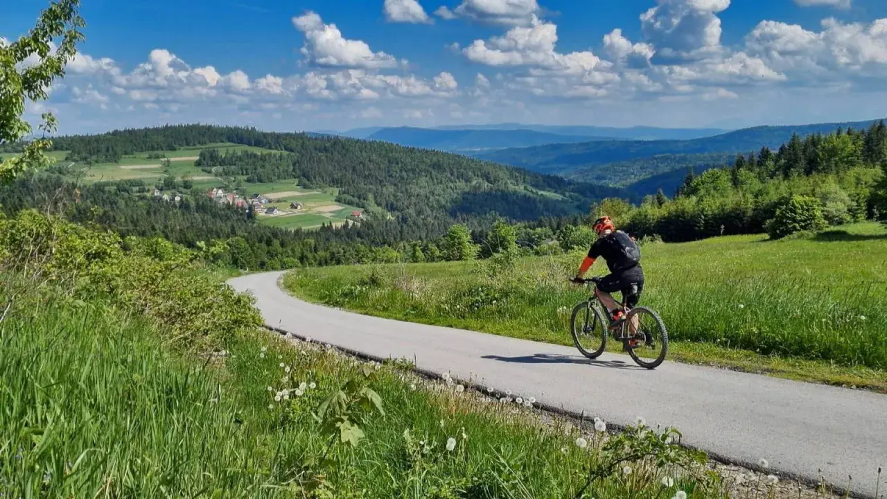 Rowerzysta na tle malowniczej **koskowej góry** i zielonych wzgórz.