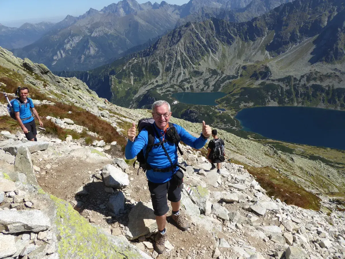 Uśmiechnięty turysta na kozi wierch trasie, z kciukiem w górze. W tle piękne Tatry i dwa jeziora.