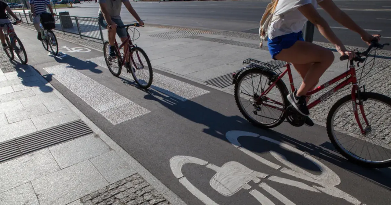 Ludzie na rowerach jadą ścieżką rowerową z oznaczeniem art 33 prd. Cienie rzucane przez rowerzystów wydłużają się na asfalcie.