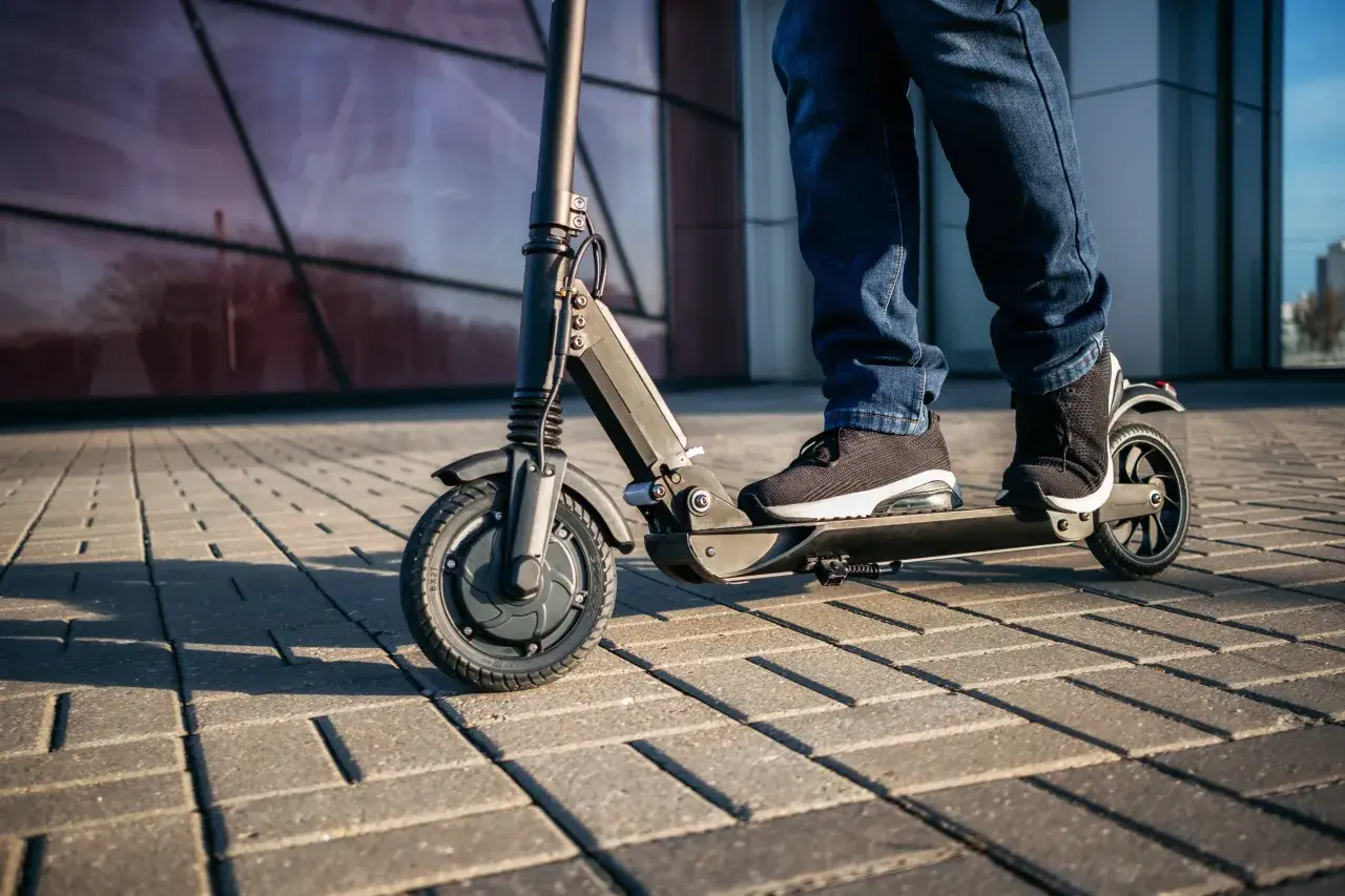 Osoba na hulajnodze elektrycznej jedzie po chodniku. Czy hulajnogą można jeździć po ścieżce rowerowej? To zależy od przepisów.
