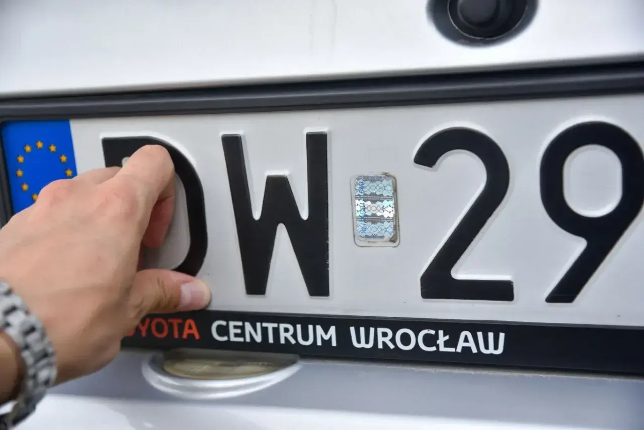 Dłoń przykłada tablicę rejestracyjną na bagażnik rowerowy. Widoczne litery DW i cyfry 29.