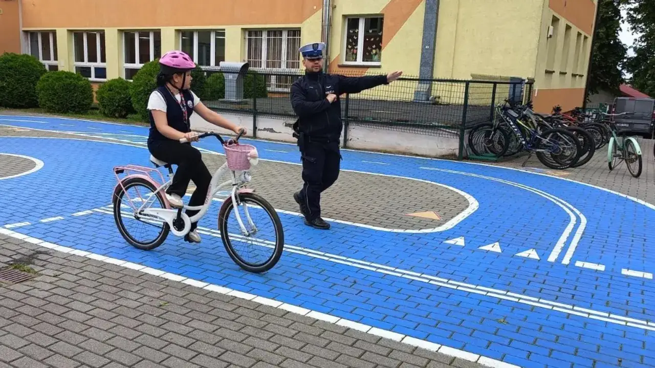 Policjant uczy dziewczynkę zasad ruchu drogowego na rowerze. Dziecko zdobywa swoje pierwsze prawo jazdy na rower.