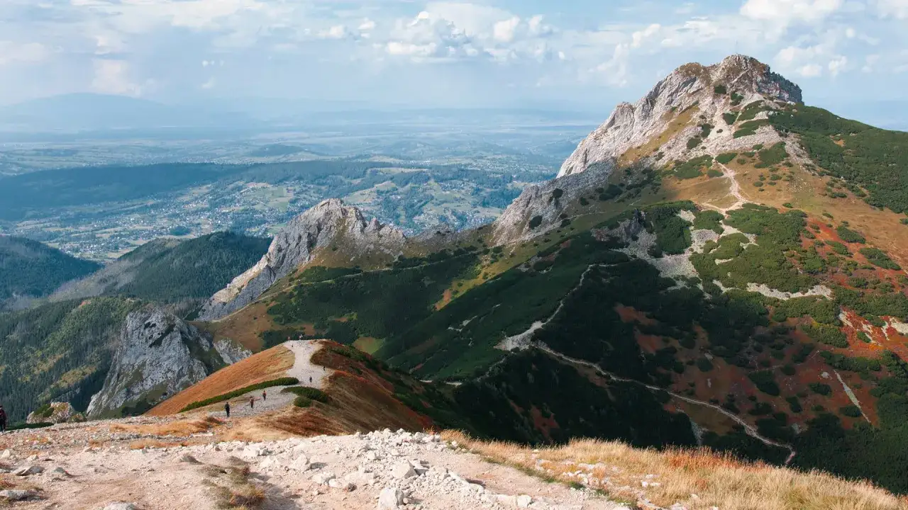 Widok z Kondrackiej Przełęczy na Tatry Zachodnie. Szlak turystyczny wije się wśród zieleni i skał, prowadząc do majestatycznego szczytu.